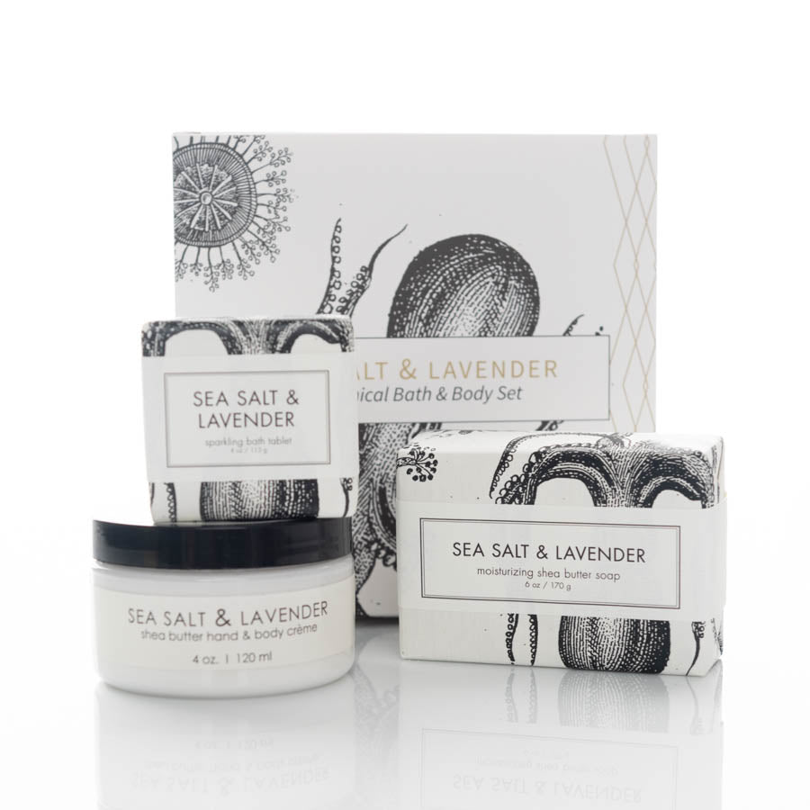 A set of skincare products labeled "Sea Salt & Lavender" arranged in front of a white background. The set includes a box labeled "Botanical Bath & Body Set," a tub of moisturizing hand & body crème, a rectangular bar of soap, and a round container of bath salts.