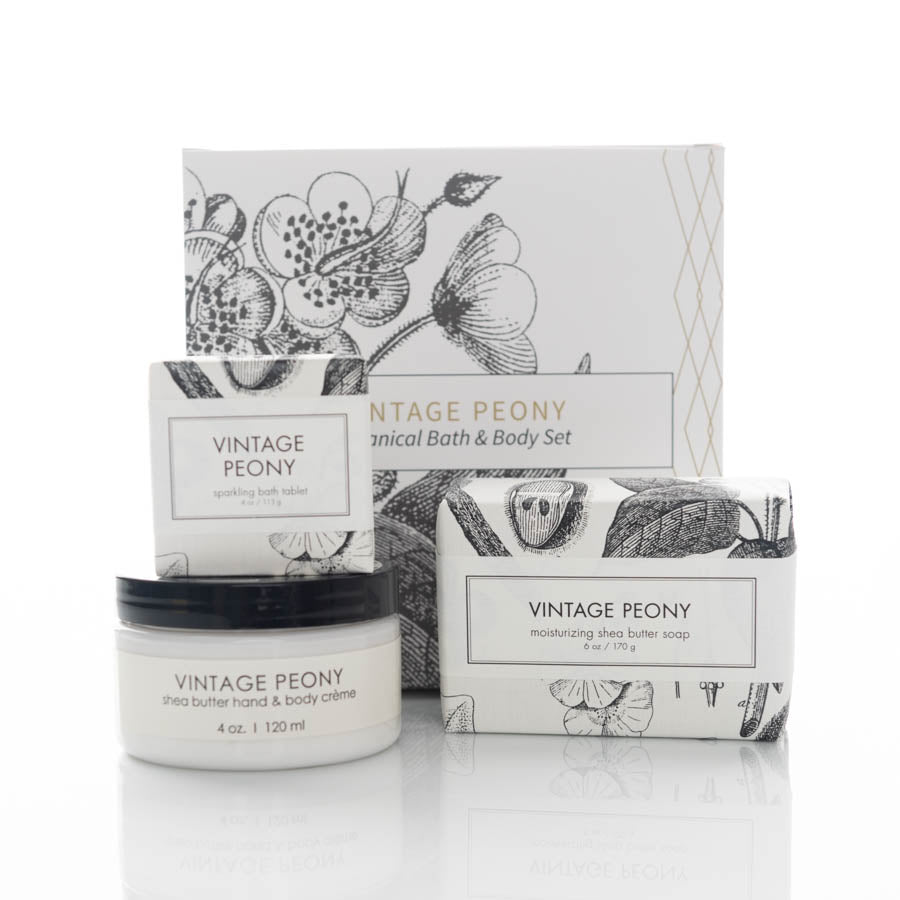 A vintage-themed bath and body set containing a small jar of shea butter hand and body creme, a bar of moisturizing shea butter soap, and a sparkling bath tablet. All items feature botanical illustrations and are packaged in coordinated white and black boxes.