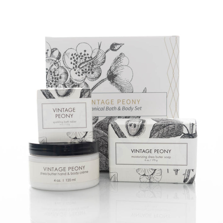 A vintage-themed bath and body set containing a small jar of shea butter hand and body creme, a bar of moisturizing shea butter soap, and a sparkling bath tablet. All items feature botanical illustrations and are packaged in coordinated white and black boxes.