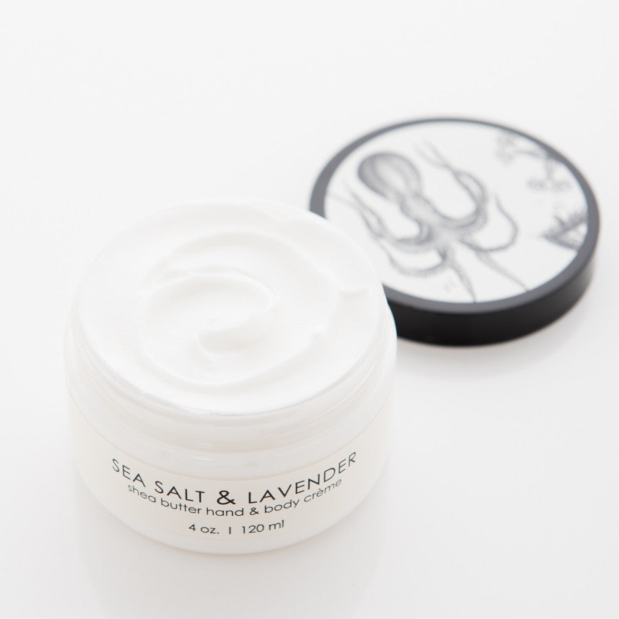 A white jar of shea butter hand and body crème labeled "Sea Salt & Lavender" with a volume of 4 oz (120 ml). The lid, placed beside the jar, features a black-and-white illustration of an octopus and flowers. The crème inside the jar is smooth and creamy.